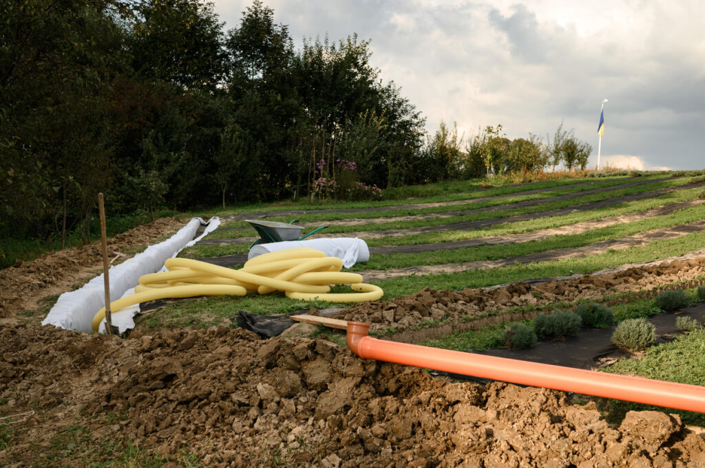 Tuyau ondulé jaune perforé dans une tranchée avec du gravier concassé et du géotextile. Travaux de drainage pour l’évacuation des eaux souterraines sur le terrain