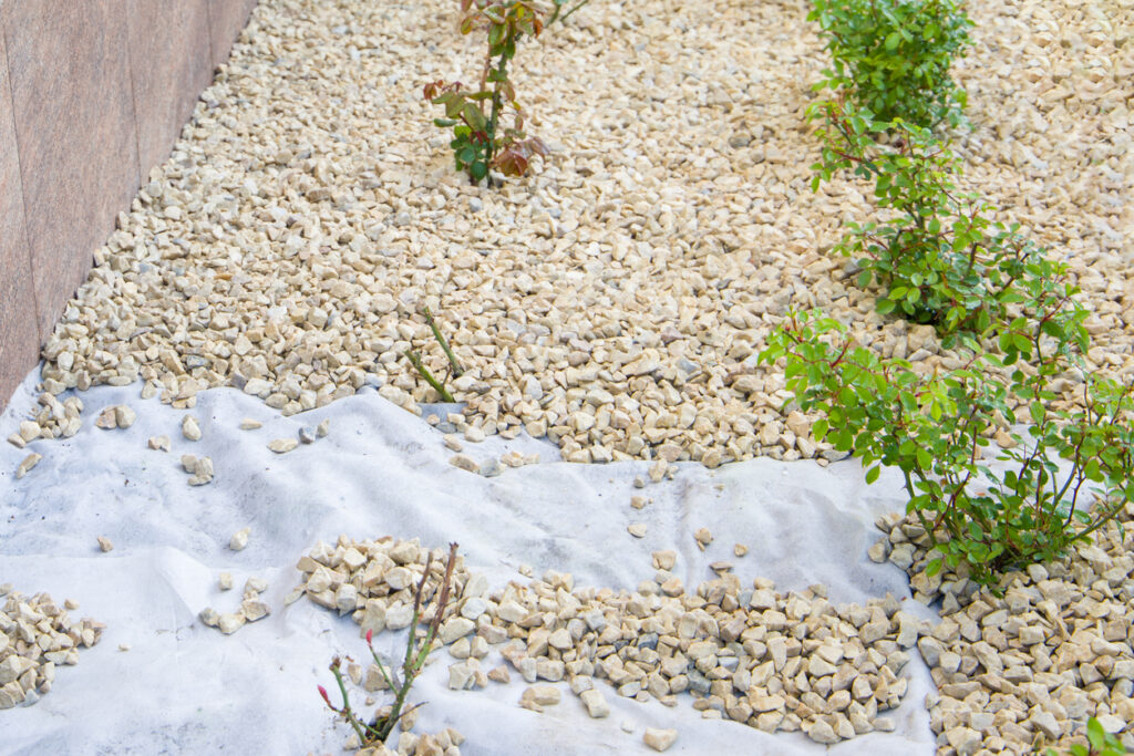 Pose de géotextile blanc et de galets sur un massif décoratif au jardin.