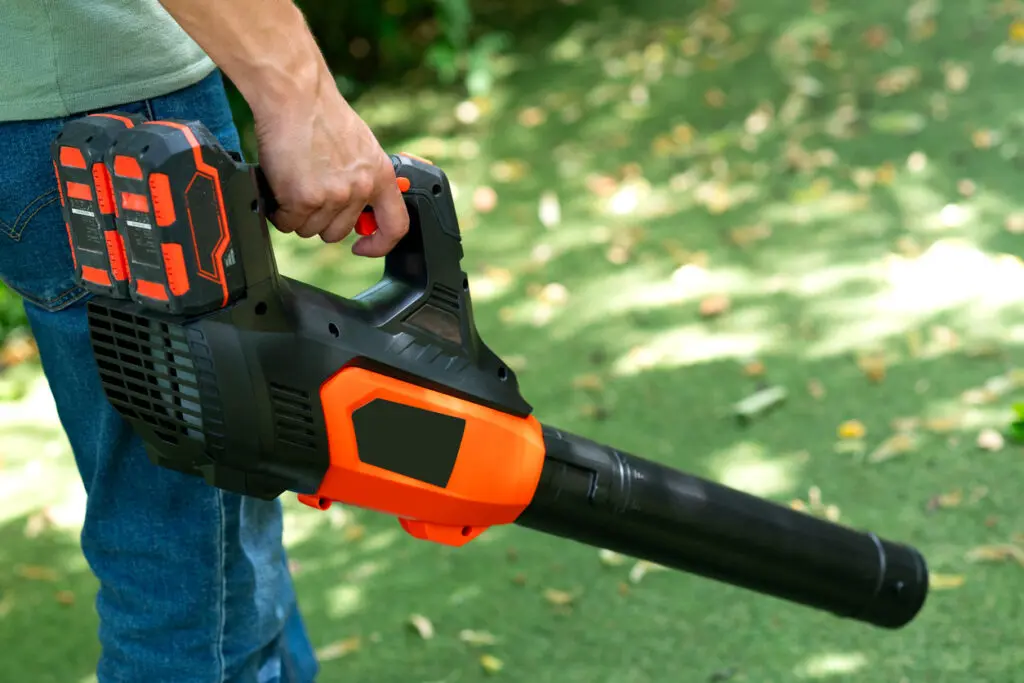 Une personne utilise un souffleur de feuilles pour enlever les feuilles mortes sur le gazon artificiel