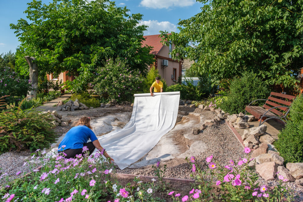 Un couple déroule un rouleau de géotextile blanc non tissé sur le sol dans leur jardin