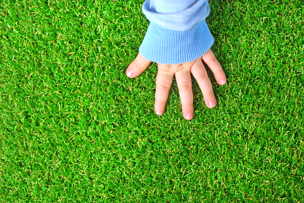 Main tendre d’un bébé sur un plancher de gazon synthétique