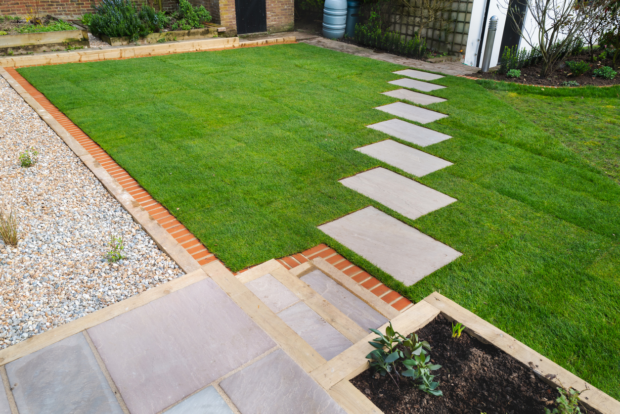 Nouvelle installation de gazon autour d'un nouveau chemin de pierres menant à une zone de galets et à un patio avec marches. Tout cela fait partie d'un projet d'aménagement paysager de jardin.